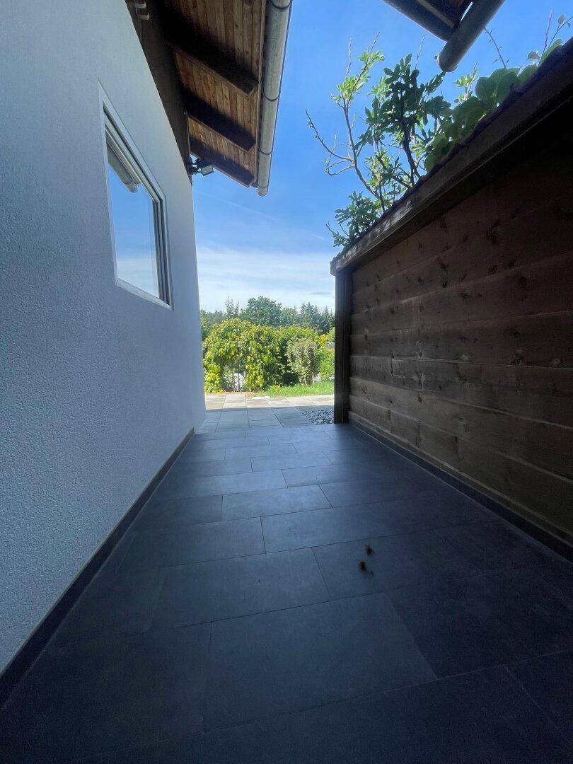 Überdachter Außenbereich mit dunklen Fliesen und Blick ins Grüne, ideal zum Entspannen.