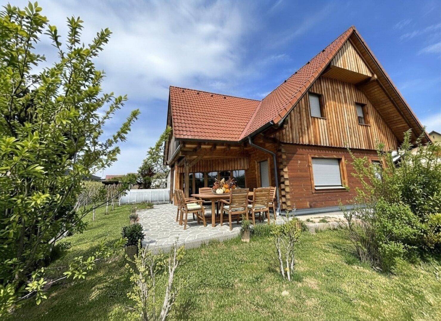 Sonnige Terrasse mit Holztisch und Stühlen, umgeben von Grünflächen.