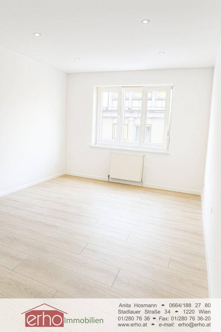 Geräumiges, helles Zimmer mit modernem Laminatboden und Blick nach draußen.