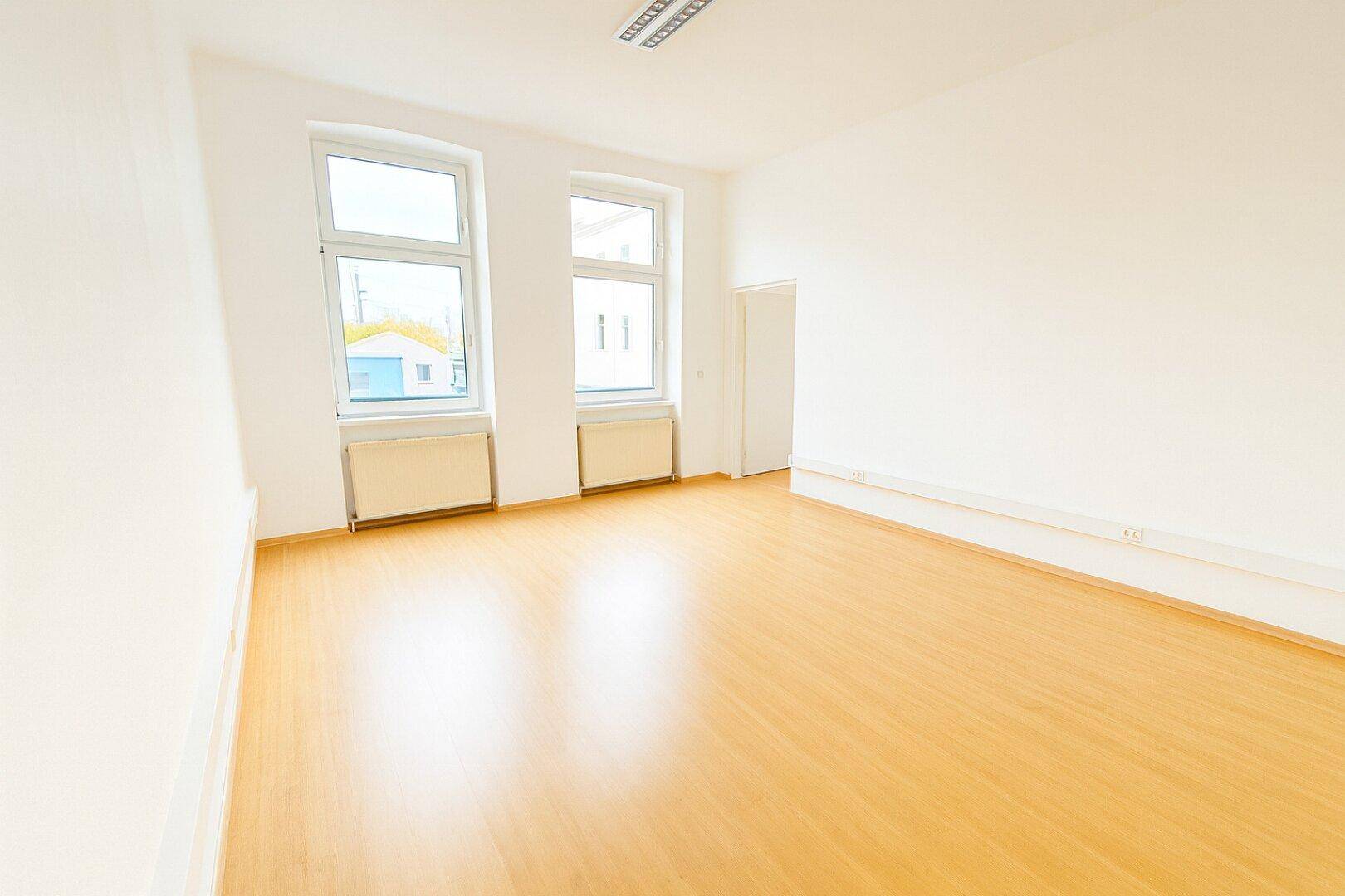 Geräumiger, heller Büroraum mit Laminatboden und großen Fenstern, bereit zur individuellen Gestaltung.