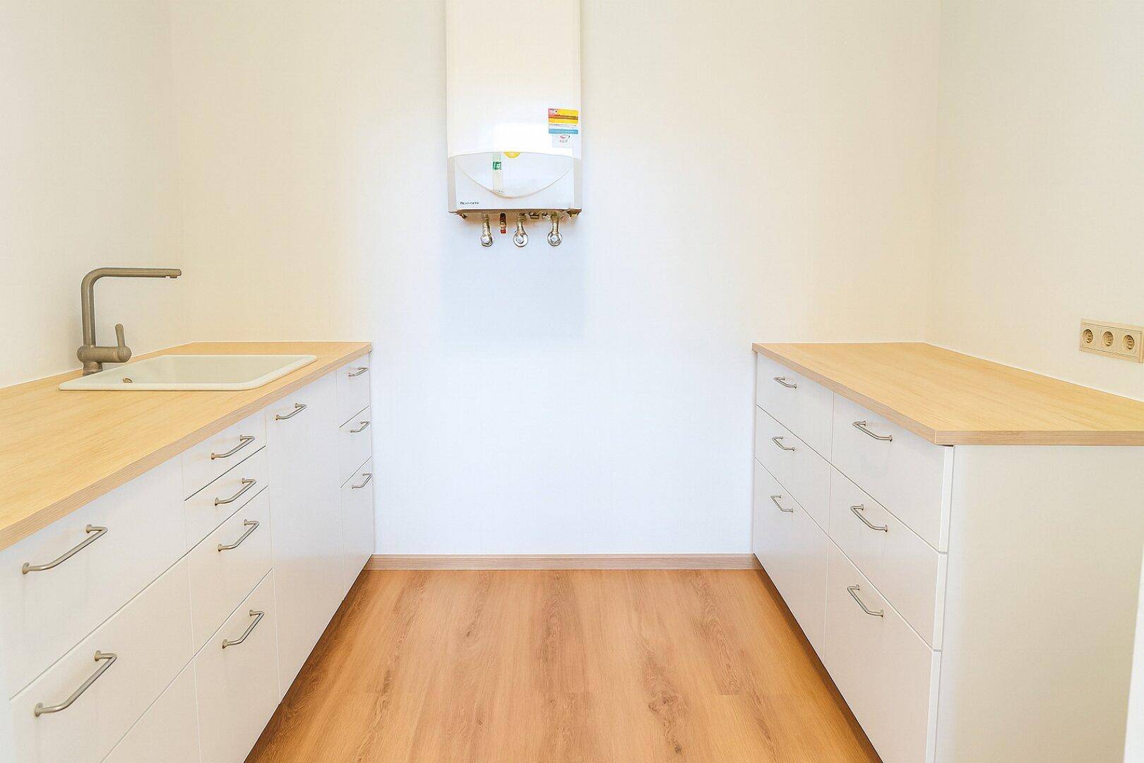 Funktionale Küchenzeile mit Holz-Arbeitsplatten, weißen Unterschränken und Gastherme an der Wand.