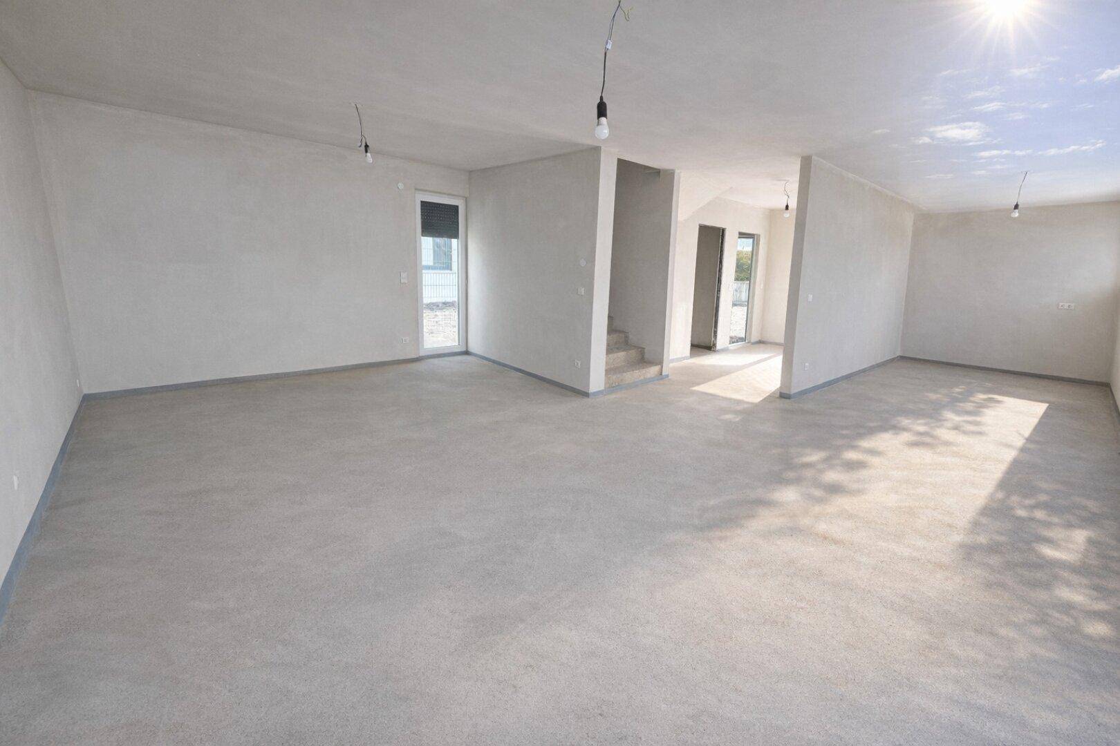 Geräumiger, unfertiger Innenraum mit Betonboden und viel natürlichem Licht, bereit für den Ausbau.