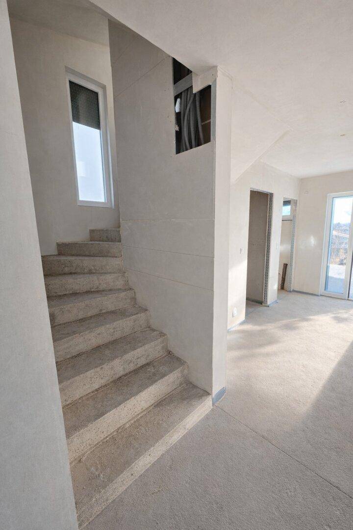 Unfertiges Treppenhaus mit Betonstufen und einem Fenster, das natürliches Licht hereinlässt.