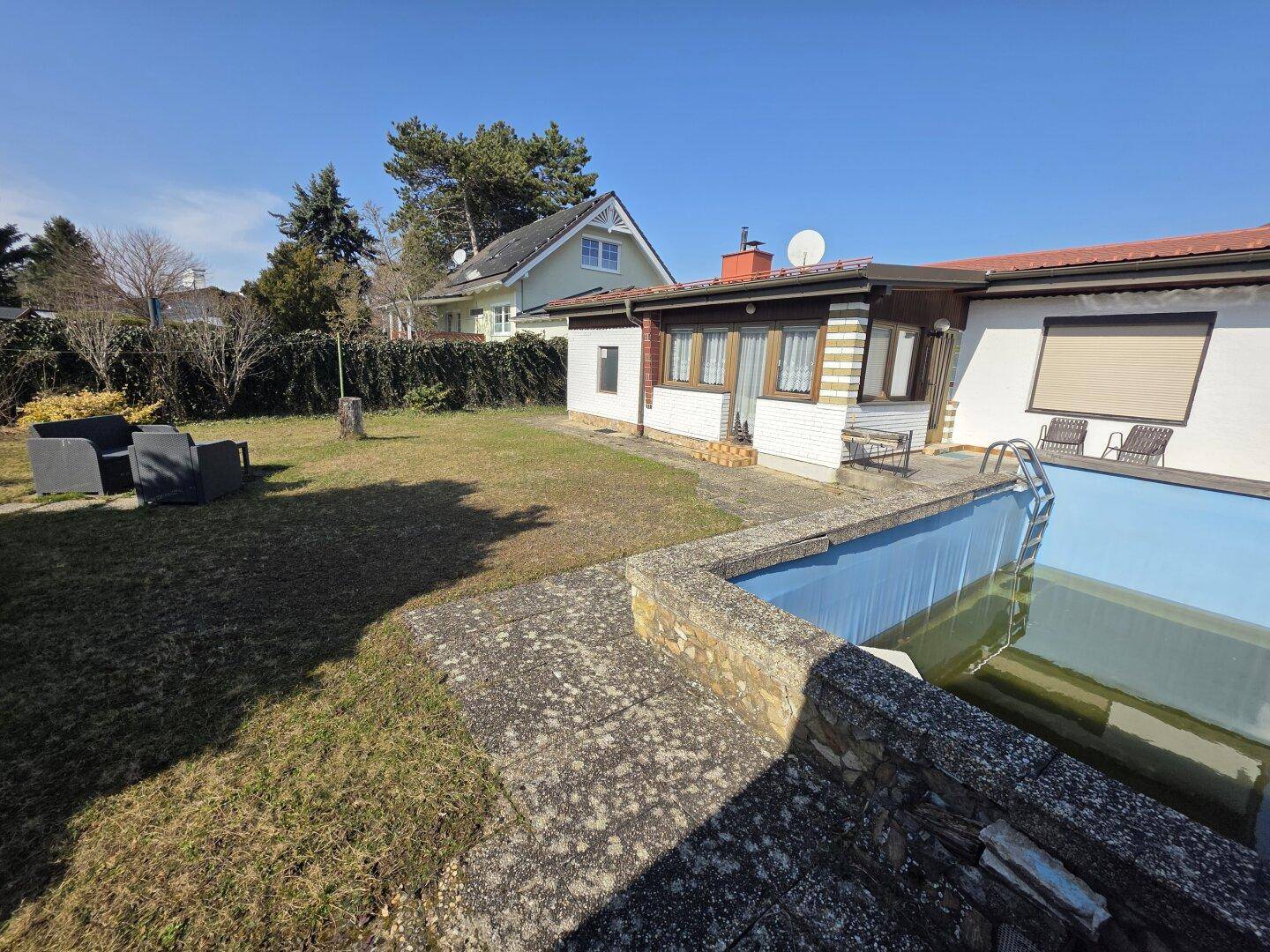 Weitläufiger Garten mit Pool, gepflasterter Terrasse und Blick auf das Nachbarhaus an einem sonnigen Tag.