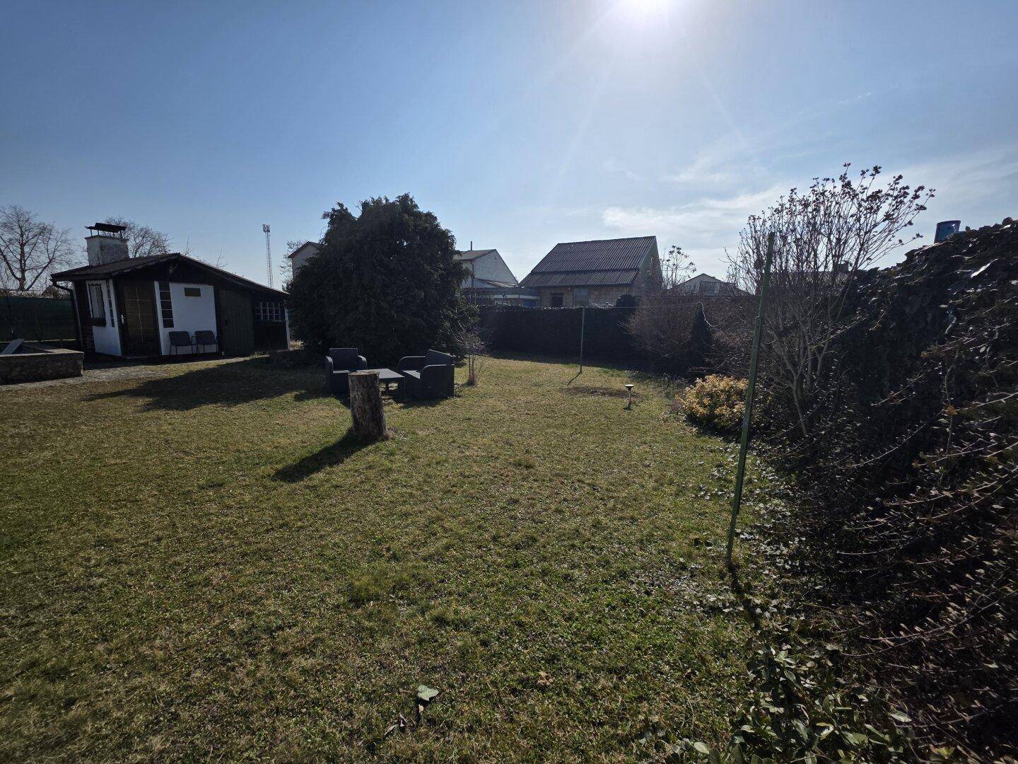 Großer, sonniger Garten mit Rasenfläche, einem Gartenhaus und Sitzgelegenheiten im Freien.