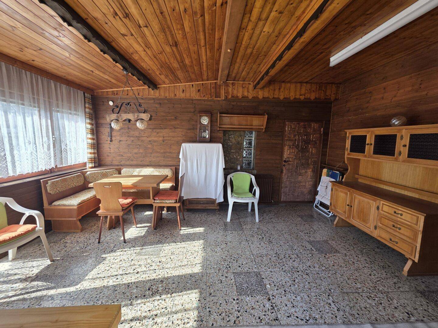 Gemütlicher Wintergarten mit Holzverkleidung, großen Fenstern und einem Essbereich.