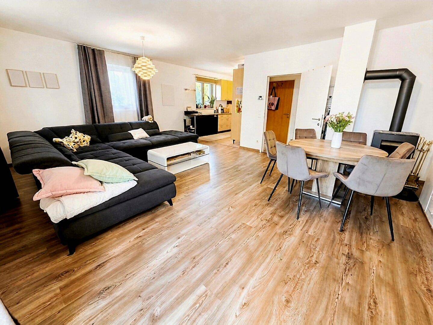 Offener Wohn- und Essbereich mit Holzboden, großem Sofa und einem gemütlichen Kaminofen.