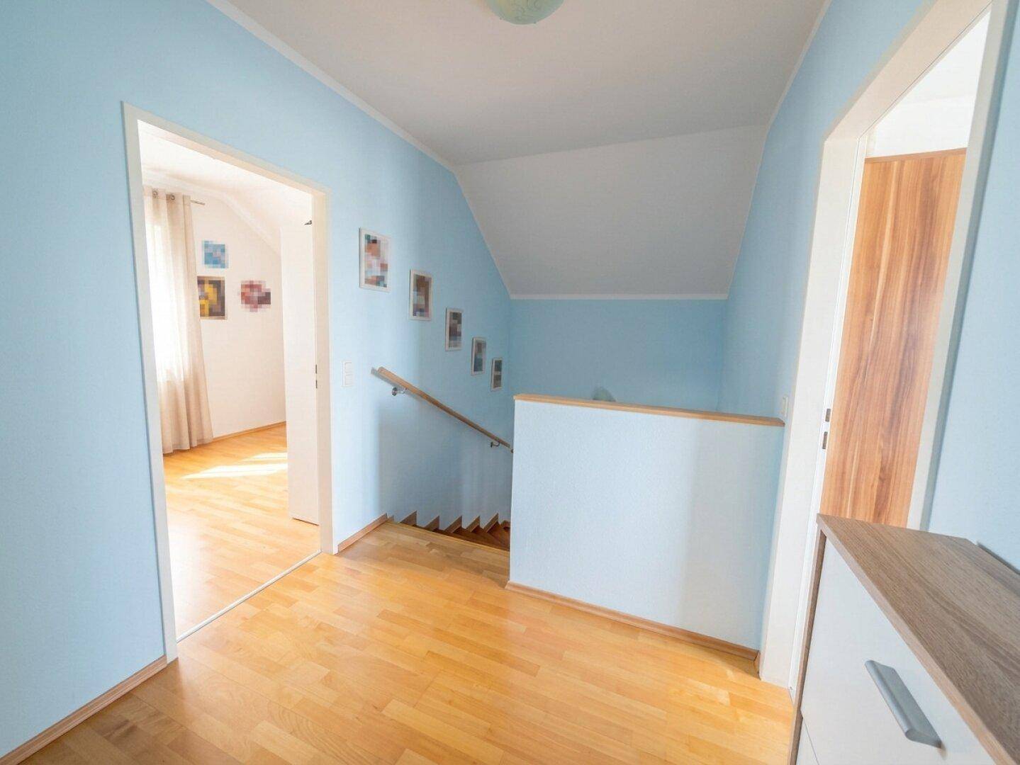 Heller Flur im Obergeschoss mit blau gestrichenen Wänden und Holzboden.