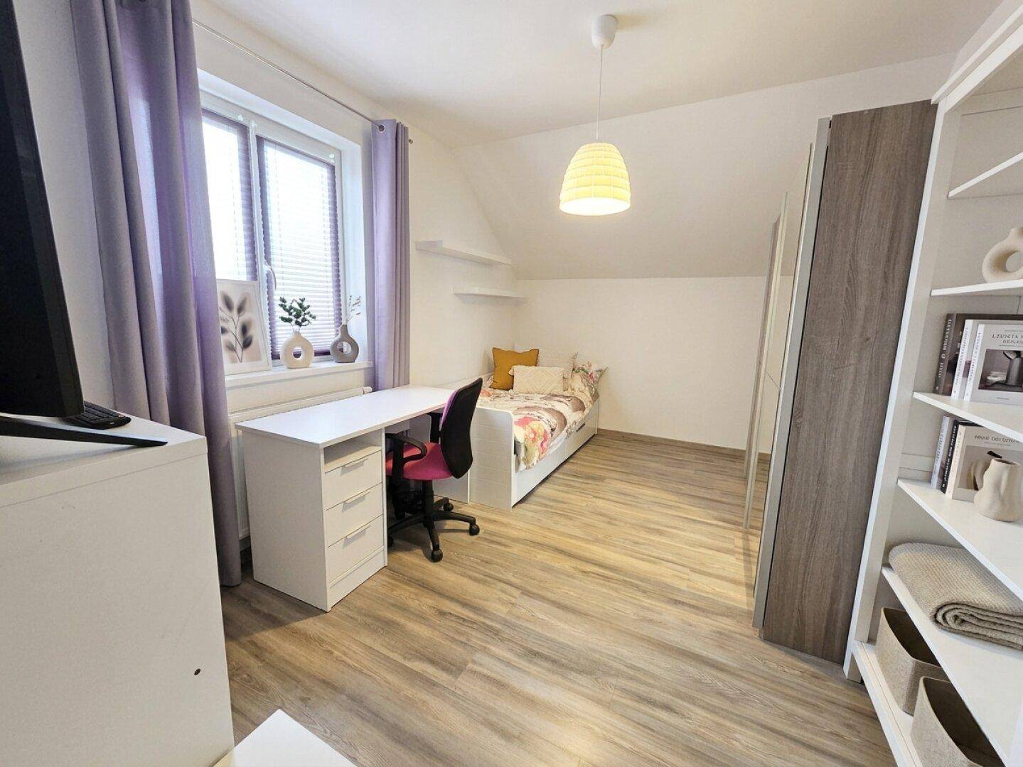 Helles Zimmer mit Dachschräge, Schreibtisch und Regal, ideal als Büro oder Gästezimmer.