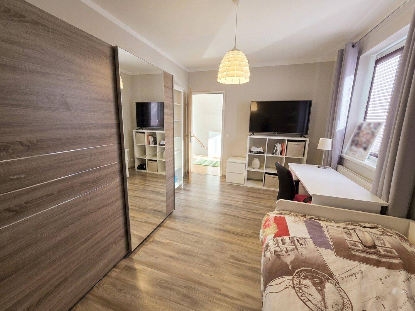 Geräumiges Zimmer mit Holzboden, großem Spiegelschrank und einem Schreibtischbereich.
