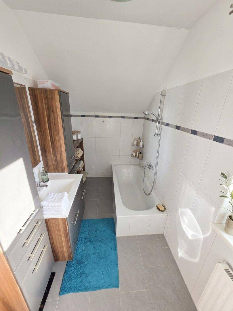 Modernes Badezimmer mit Badewanne, Waschtisch und hellen Fliesen unter der Dachschräge.