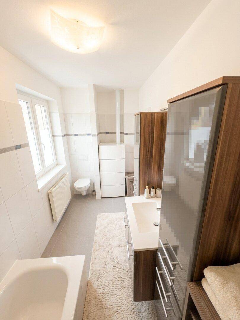 Helles Badezimmer mit Fenster, Badewanne, Waschtisch und modernen Holzschränken.