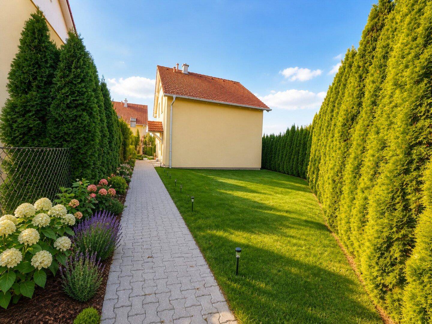 Gepflegter Gartenweg zwischen hohen Hecken und blühenden Blumenbeeten.