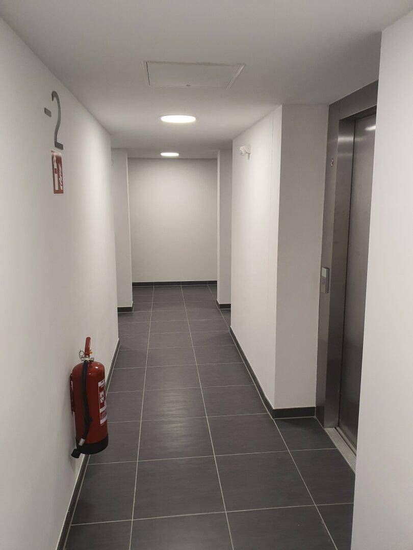 Heller Flur mit Aufzug, dunklen Fliesen und weiß gestrichenen Wänden im Gebäude.