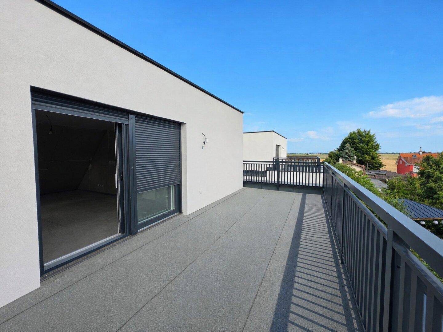 Geräumige Dachterrasse mit Metallgeländer und Schiebetür, bietet einen weiten Ausblick.