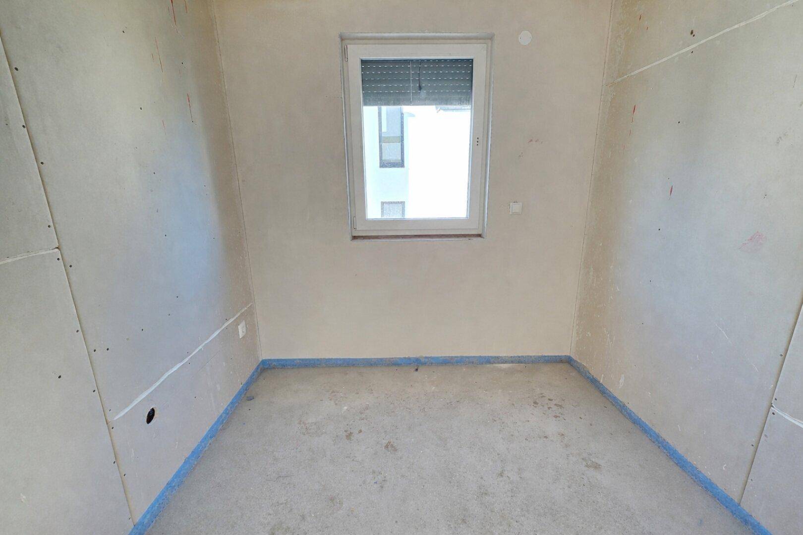 Leerer Raum im Rohbauzustand mit Fenster und Rollladen, bereit für den Ausbau.