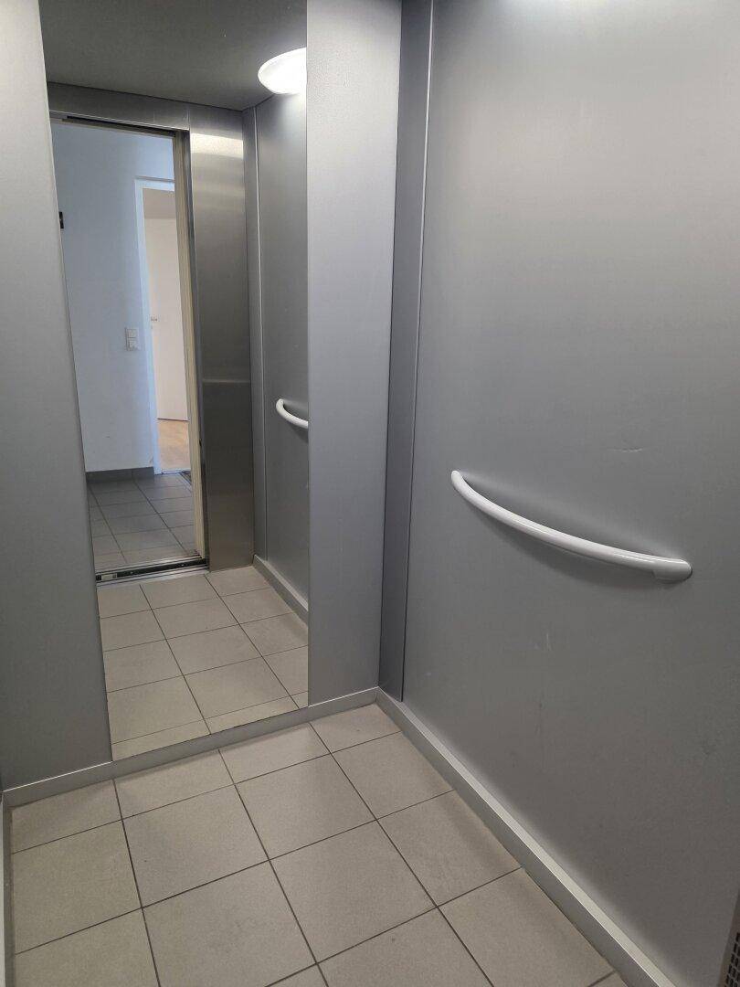 Moderner Aufzug mit Spiegel, Haltegriffen und Fliesenboden im Gebäude.