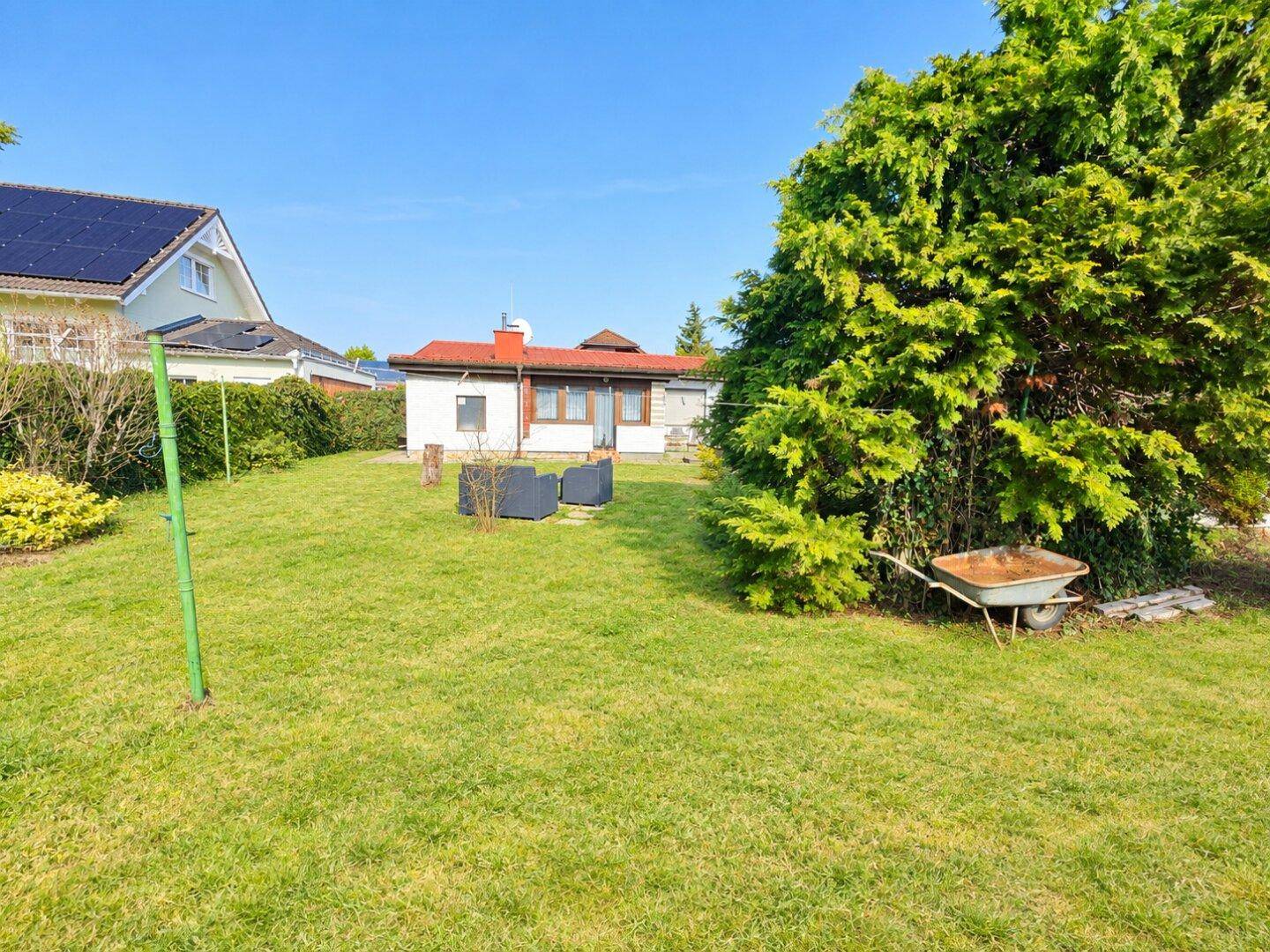 Weitläufiger Garten mit Rasenfläche, Bäumen und Blick auf das Haus unter strahlendem Sonnenschein.