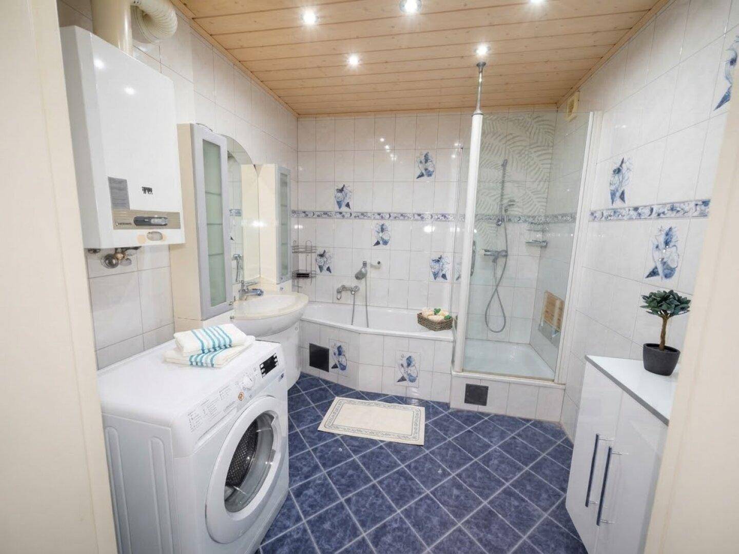 Badezimmer mit Badewanne, Dusche, Waschmaschine und blauen Bodenfliesen.