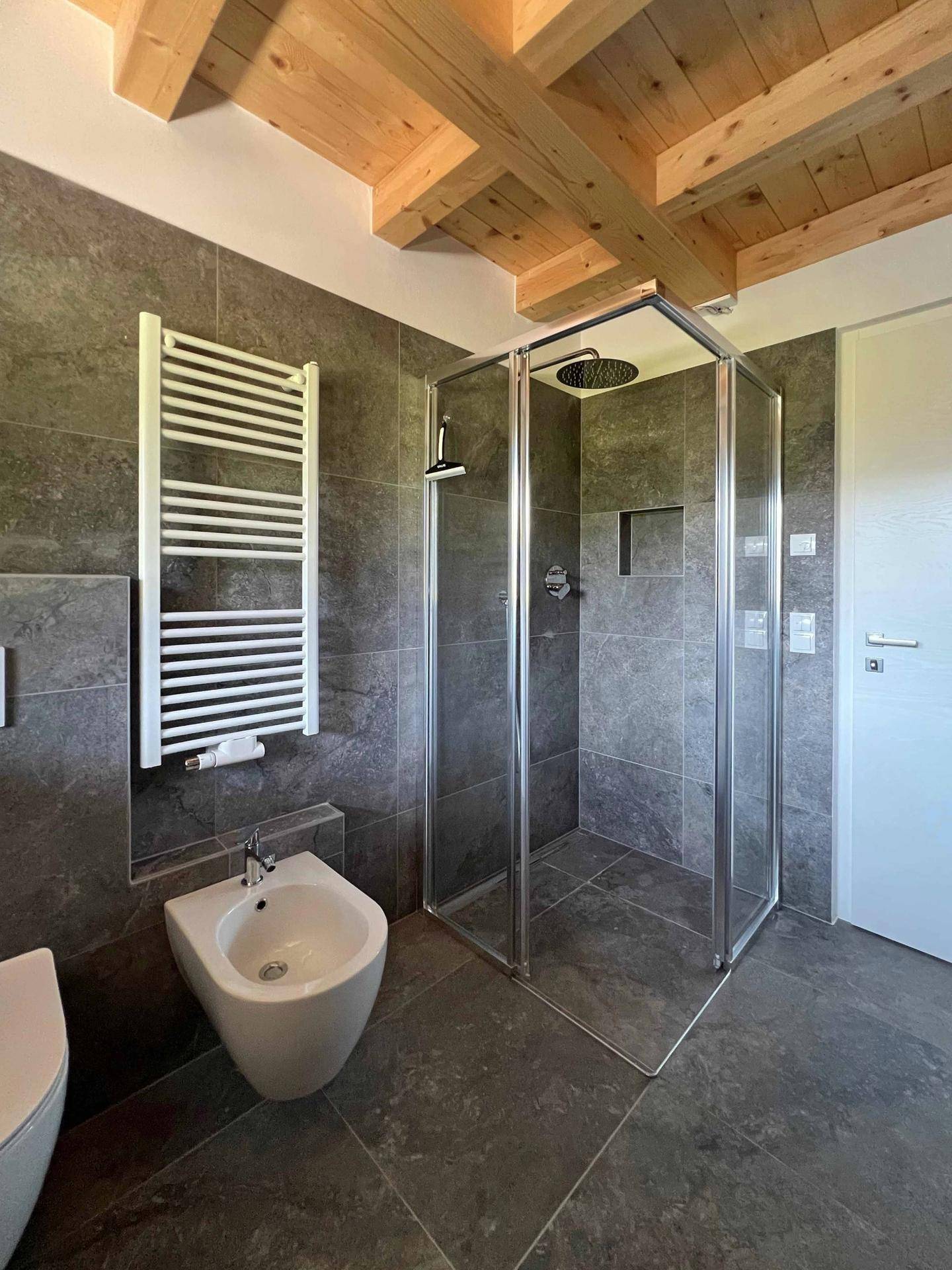 Elegantes Badezimmer mit begehbarer Dusche, Bidet, beheiztem Handtuchhalter und Holzbalkendecke.