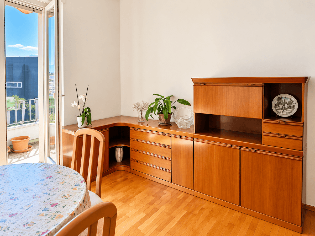 Essbereich mit elegantem Holz-Sideboard, Pflanzen und Zugang zu einem sonnigen Außenbereich.