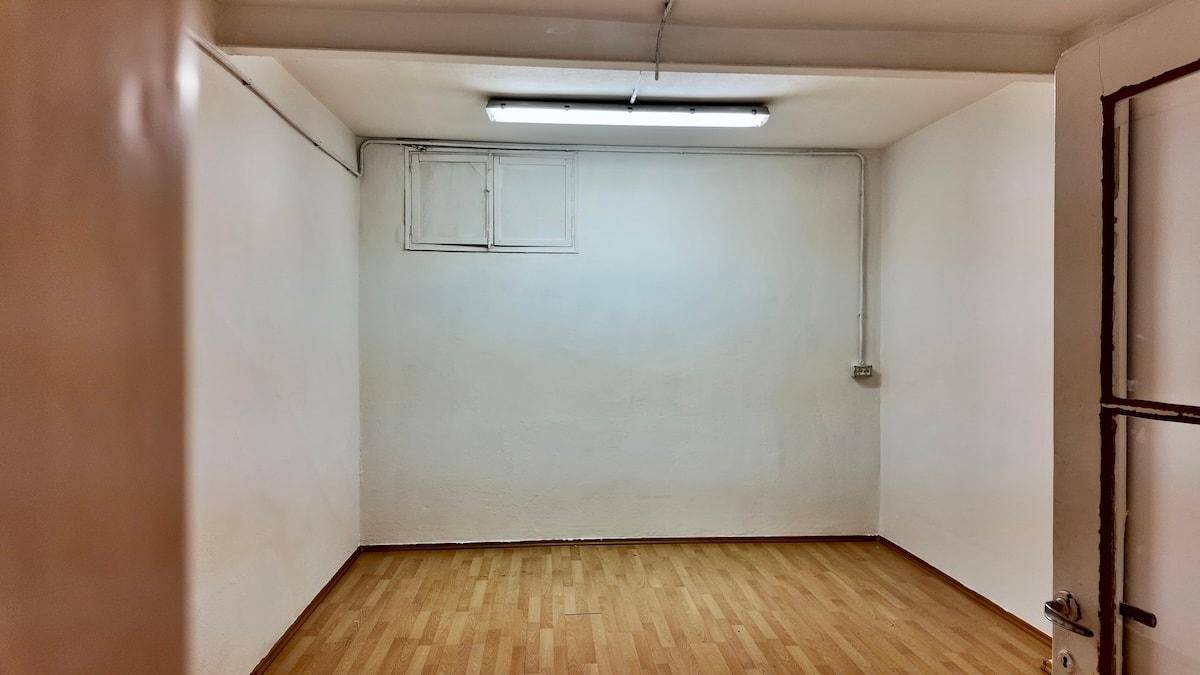 Leerer Kellerraum mit Holzfußboden, weißen Wänden und einer Deckenleuchte.