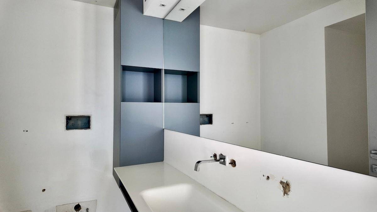 Modernes Badezimmer mit Einzelwaschbecken, großem Spiegel und grauem Einbauschrank, noch im Bau.