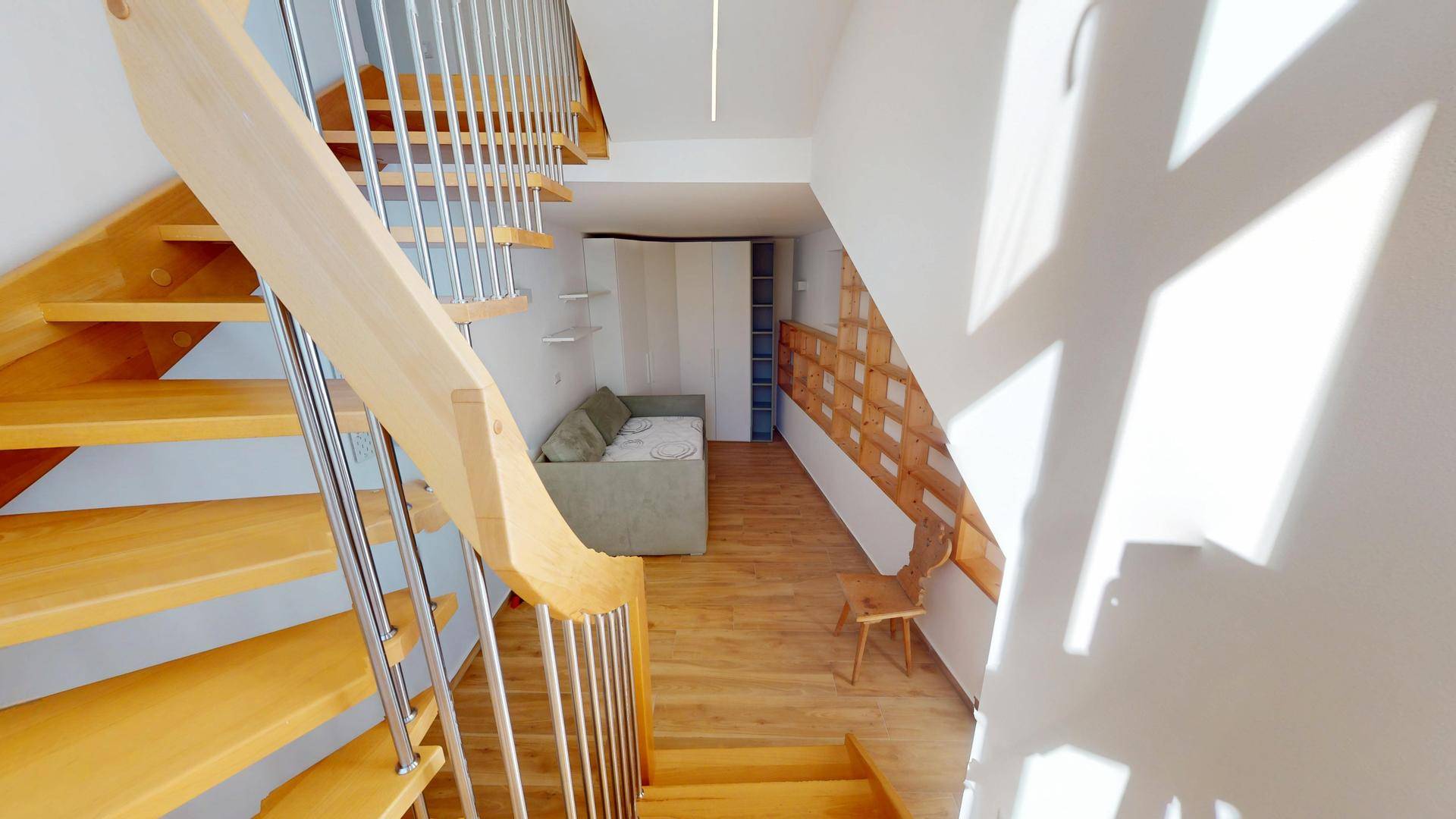 Holztreppe mit Metallgeländer führt zu einem gemütlichen Bereich mit Schlafsofa und Regalen.