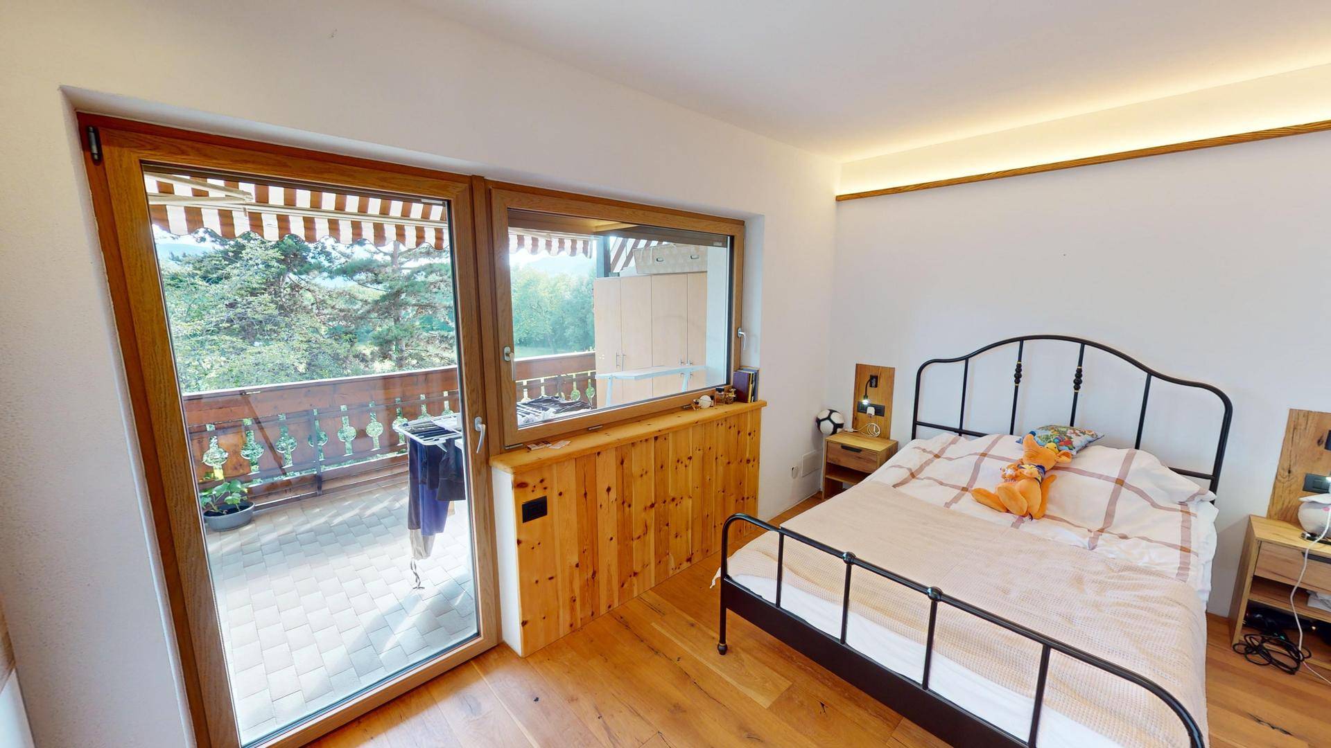 Schlafzimmer mit Balkonzugang, Holzboden und Blick auf die umliegende Landschaft.