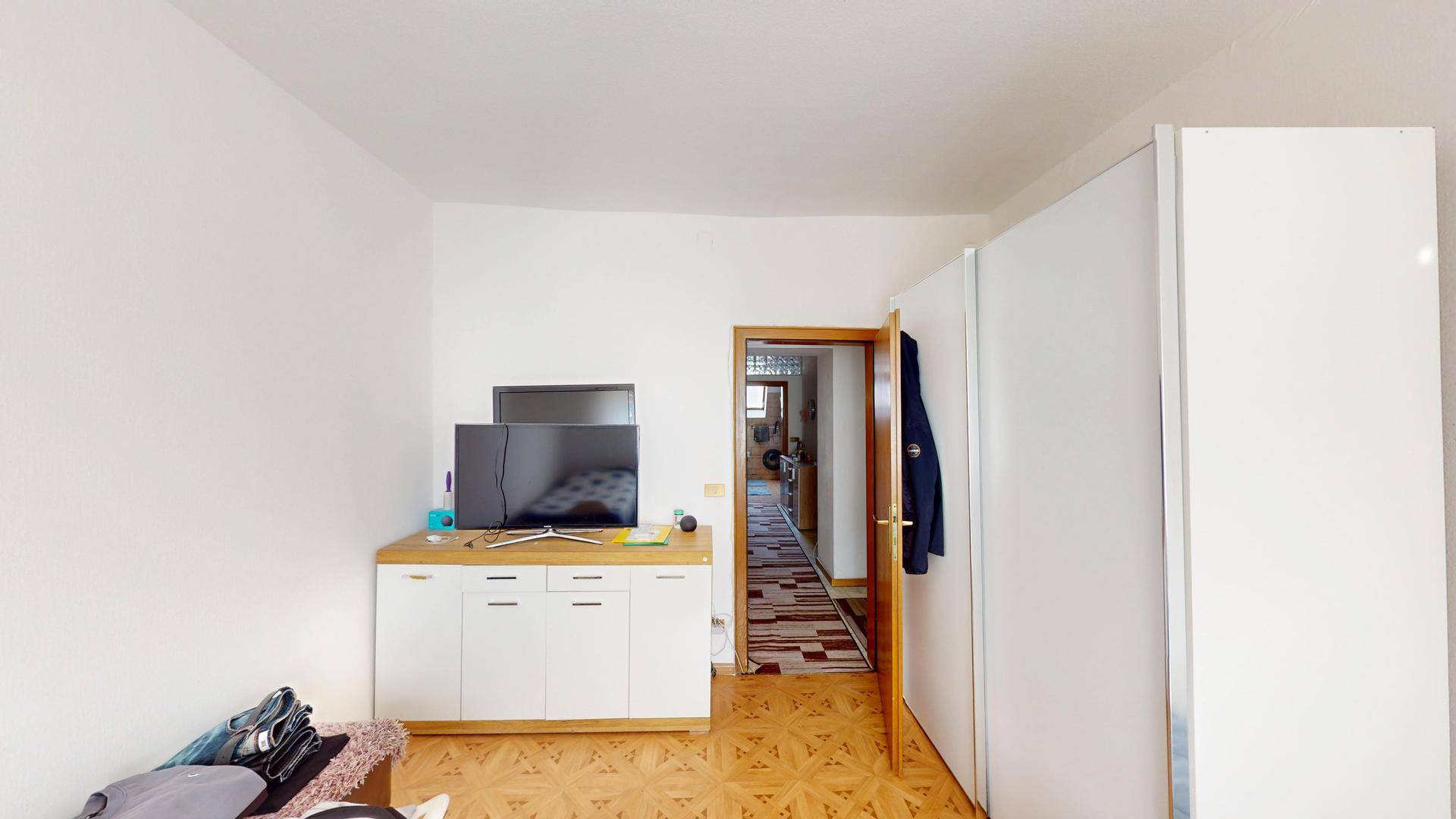 Schlafzimmer mit Fernseher, Kommode und einem offenen Durchgang zu einem Flur.