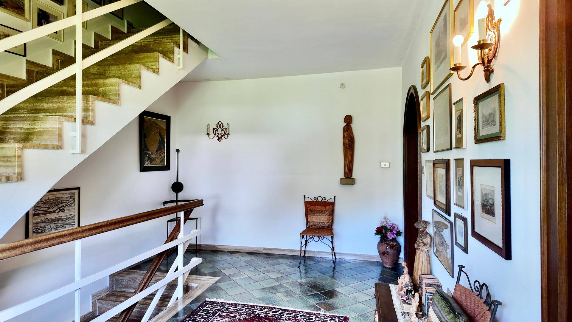 Geräumiger Eingangsbereich mit Treppe, Fliesenboden und Kunstwerken an den Wänden, hell beleuchtet.