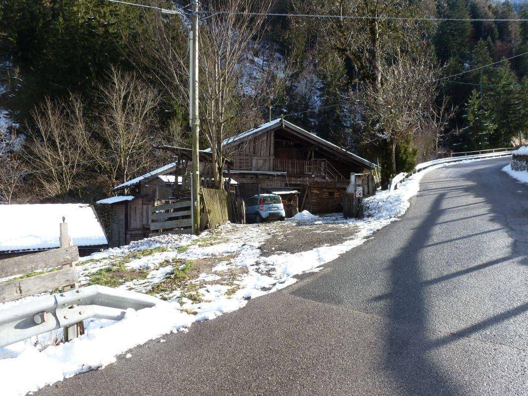 Gesamtansicht des Holzhauses in einer verschneiten Berglandschaft mit Zufahrtsstraße und geparktem Auto.