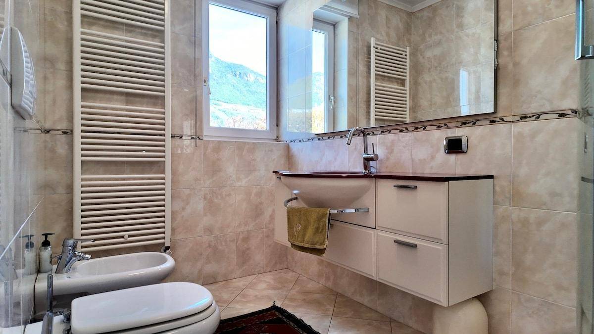 Badezimmer mit beigefarbenen Fliesen, Bidet, WC und Fenster.