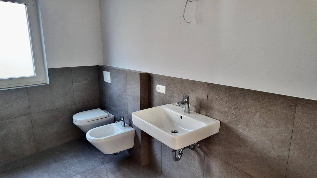 Modernes Badezimmer mit grauen Fliesen, wandhängendem WC, Bidet und Einzelwaschbecken.