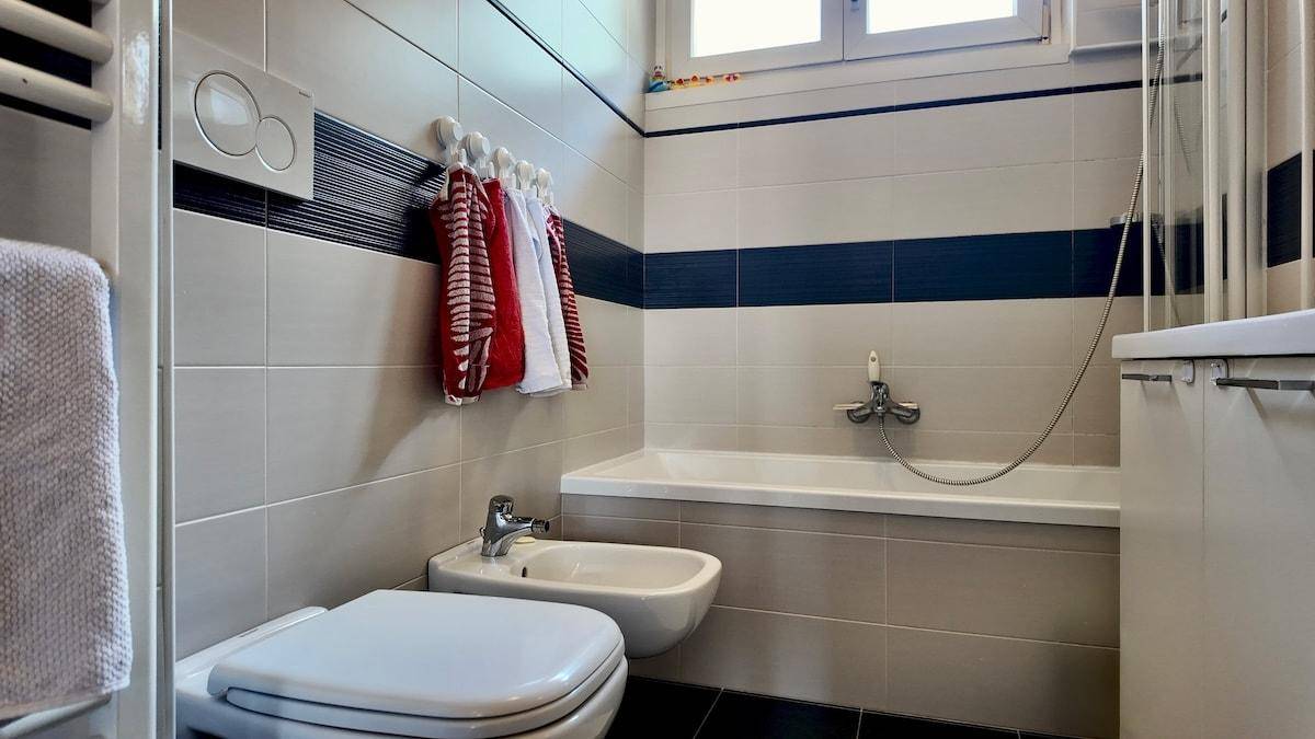 Modernes Badezimmer mit Badewanne, WC, Bidet und Fliesen in Grau und Dunkelblau.