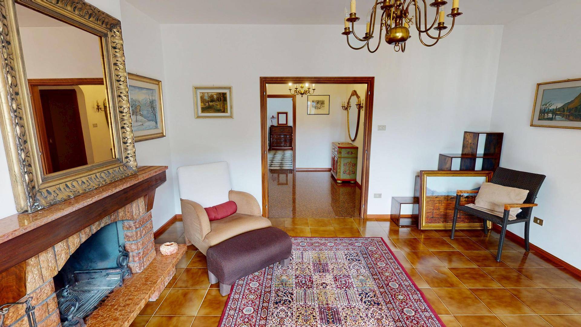Wohnzimmer mit Kamin, Fliesenboden und Durchgang zu einem weiteren Raum mit klassischer Einrichtung.