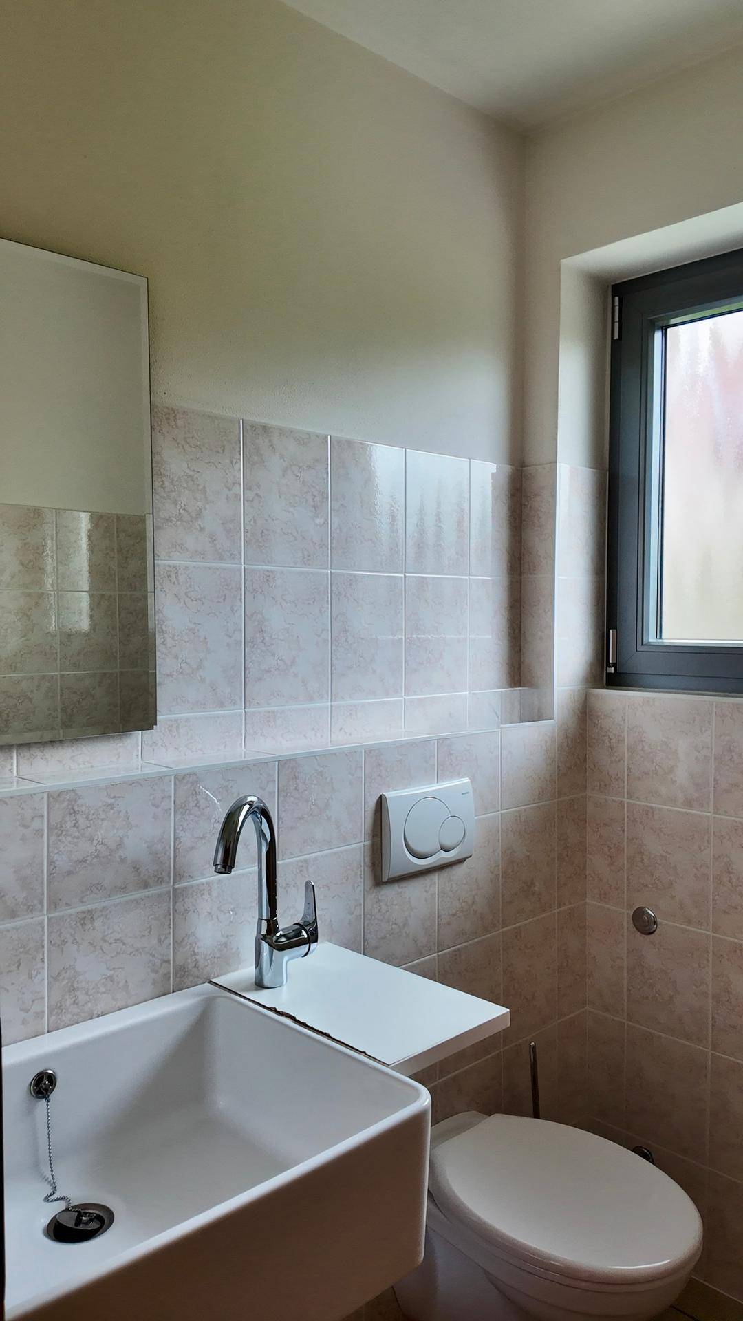 Modernes Badezimmer mit Waschbecken, Toilette, Spiegel und einem Fenster für natürliches Licht.
