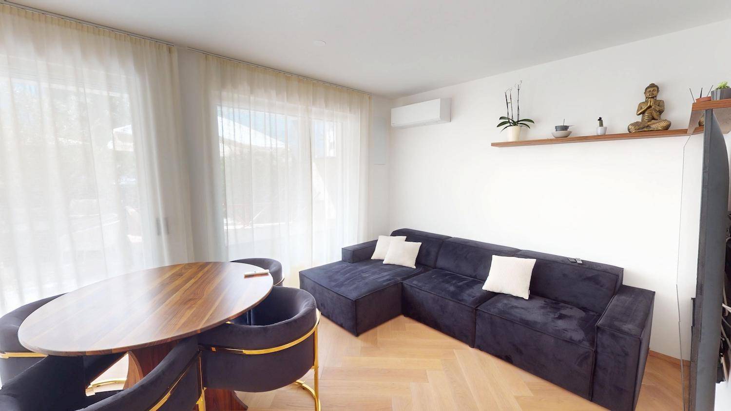 Gemütliches Wohnzimmer mit großem Sofa, Esstisch und viel Tageslicht durch die Fenster.