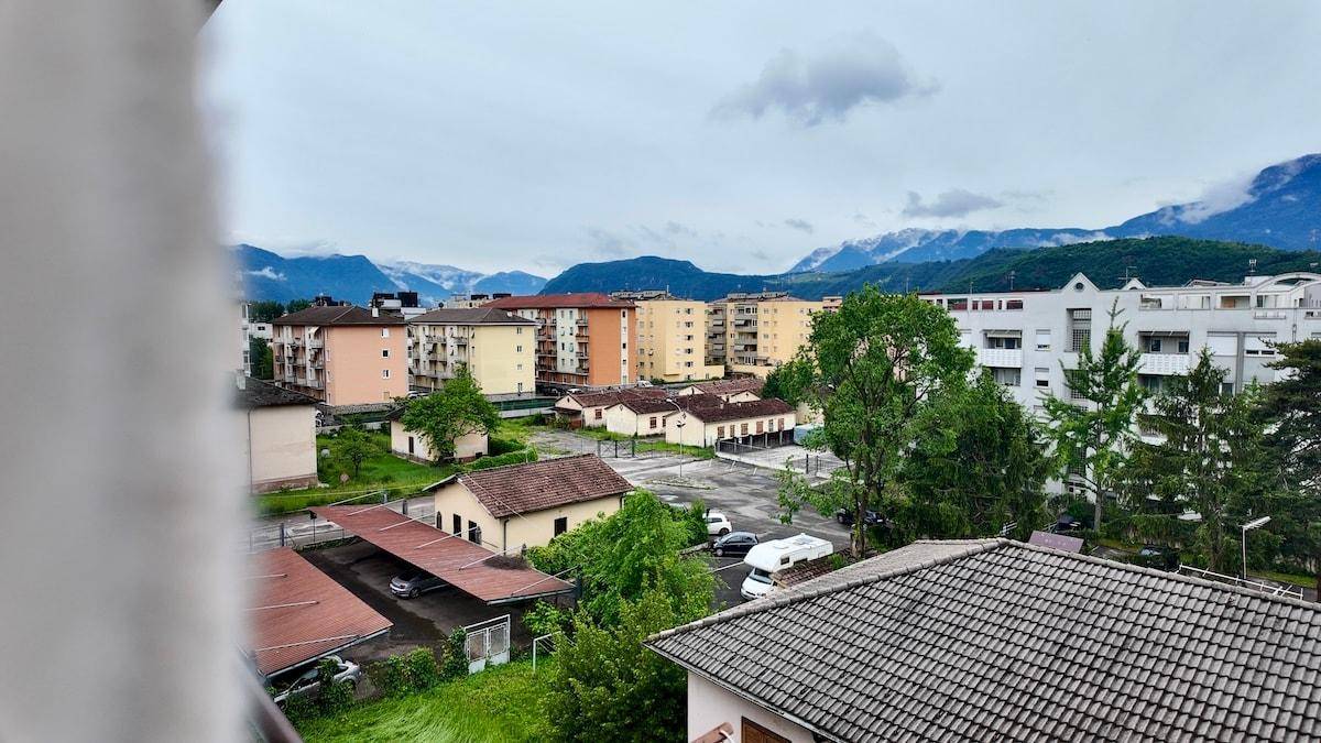 Weitblick von einem Balkon über Wohngebäude, Bäume und die Berglandschaft.
