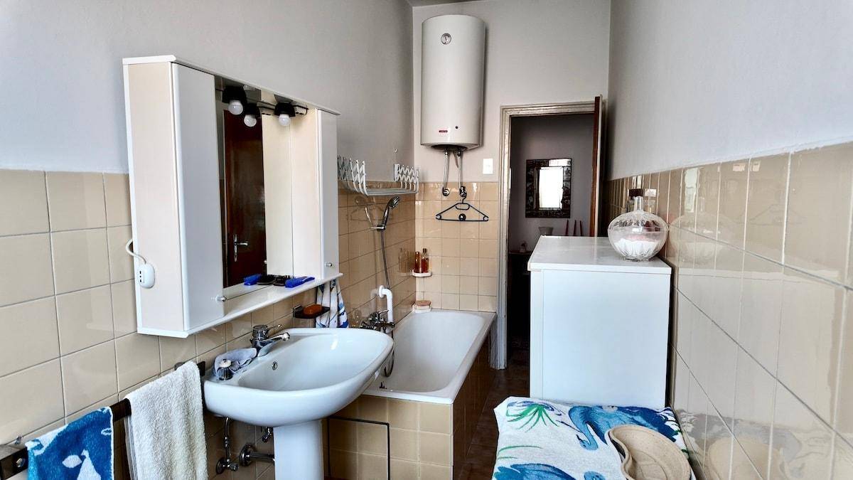 Badezimmer mit Waschbecken, Badewanne und einem Warmwasserbereiter an der Wand.