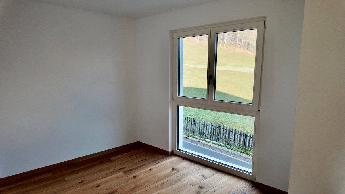 Heller Raum mit Holzboden und großem Fenster, das einen Blick ins Grüne bietet.