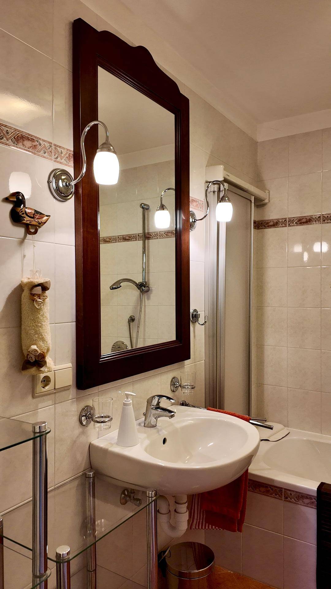 Detailansicht des Badezimmers mit Waschbecken, großem Spiegel und dekorativen Fliesen.