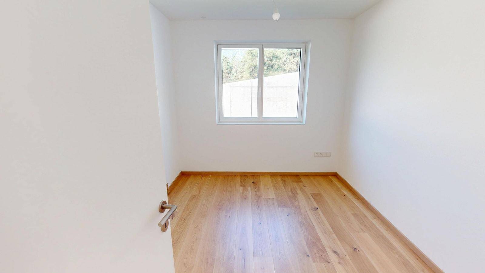 Helles, leeres Zimmer mit Holzboden und einem Fenster, ideal als Schlaf- oder Arbeitszimmer.