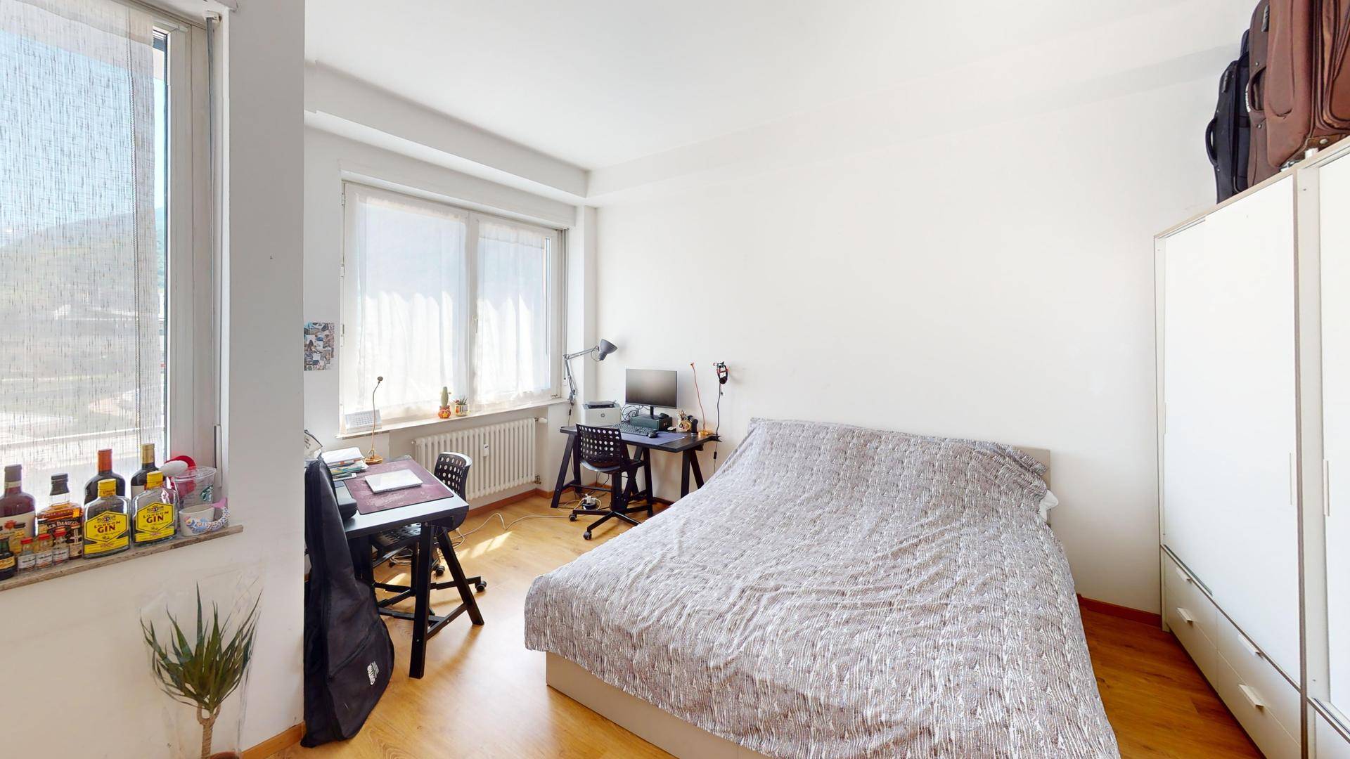 Schlafzimmer mit Holzboden, Doppelbett und Arbeitsbereich am Fenster.