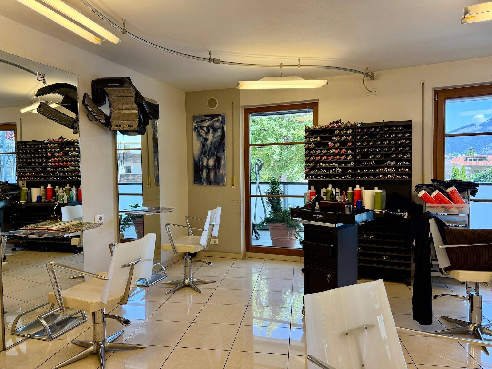 Friseursalon mit mehreren Arbeitsplätzen, Produktregalen und einem Fenster mit Ausblick.