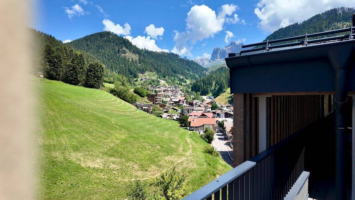 Malerischer Ausblick vom Balkon auf ein idyllisches Dorf im grünen Tal, umgeben von majestätischen Bergen.