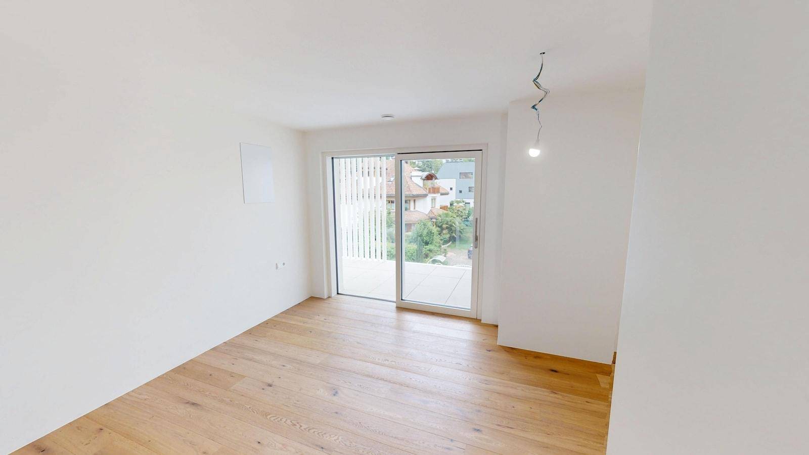 Geräumiges Zimmer mit hellem Parkettboden und Schiebetür zu einem Außenbereich mit Blick ins Grüne.