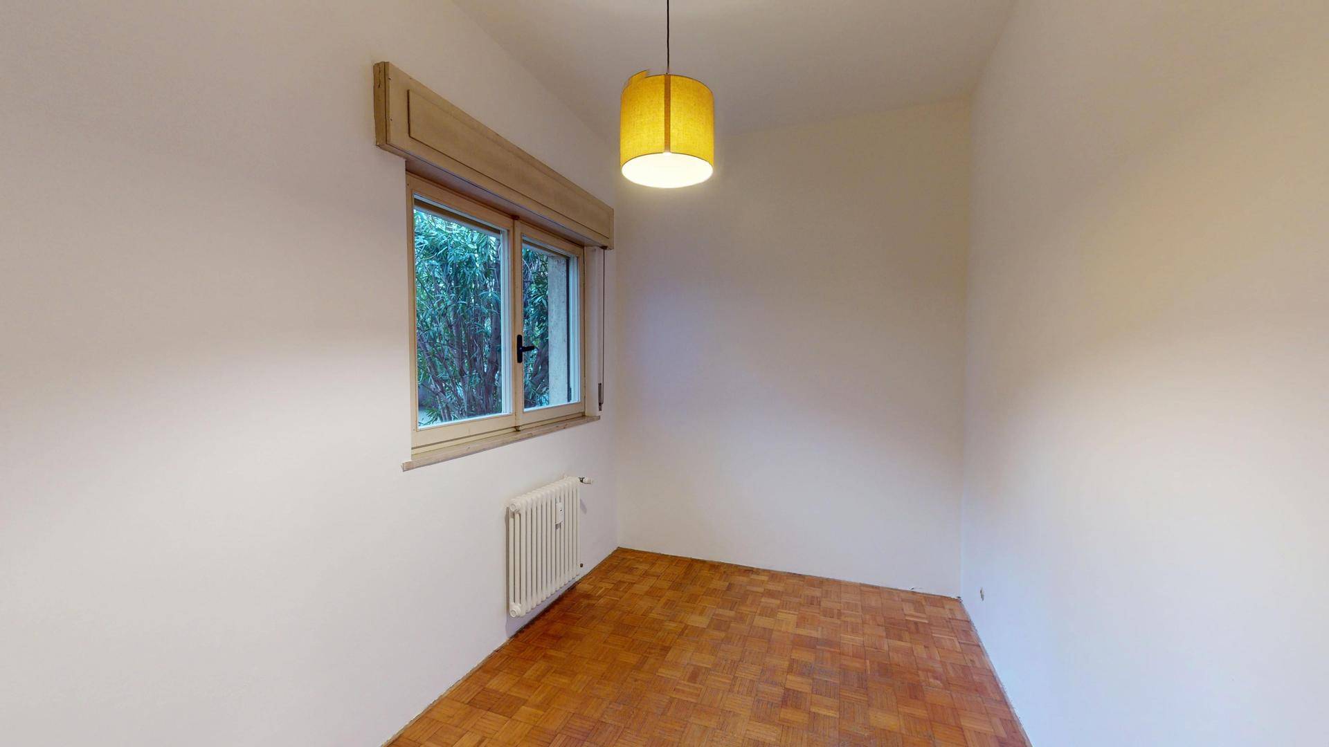 Helles Zimmer mit Parkettboden und einem Fenster, das einen angenehmen Blick ins Grüne bietet.