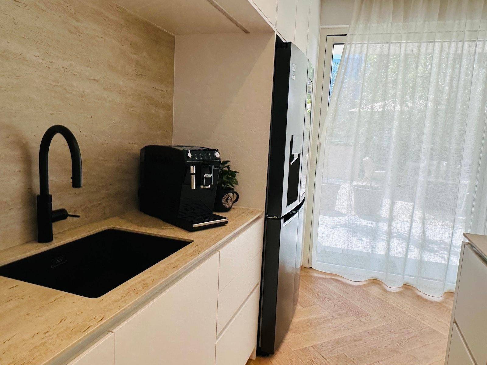 Detailansicht der modernen Küche mit schwarzer Spüle, Kaffeemaschine und großem Fenster.