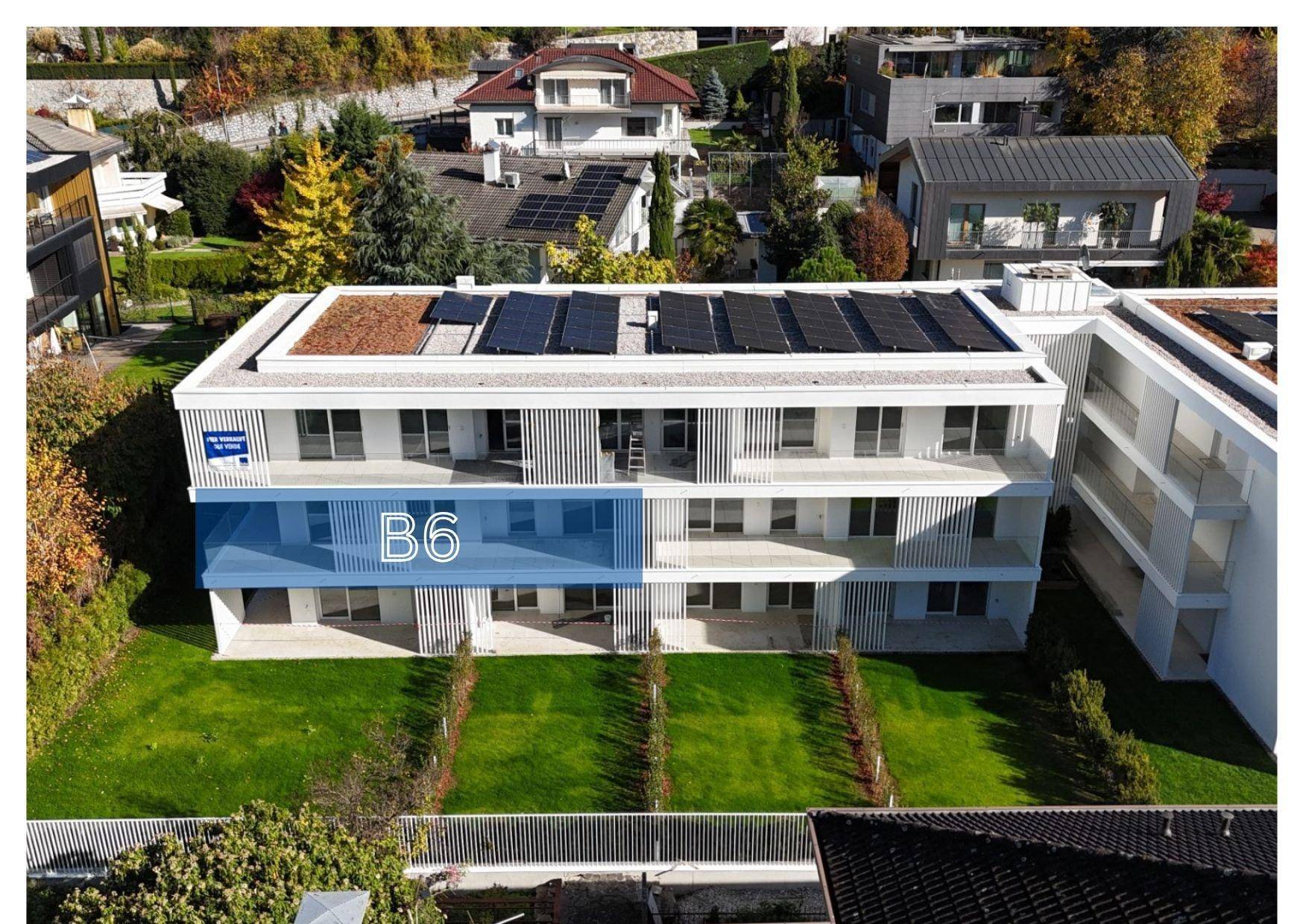 Moderne Wohnanlage mit Flachdach, Photovoltaikanlage und gepflegten Grünflächen in einer Wohngegend.